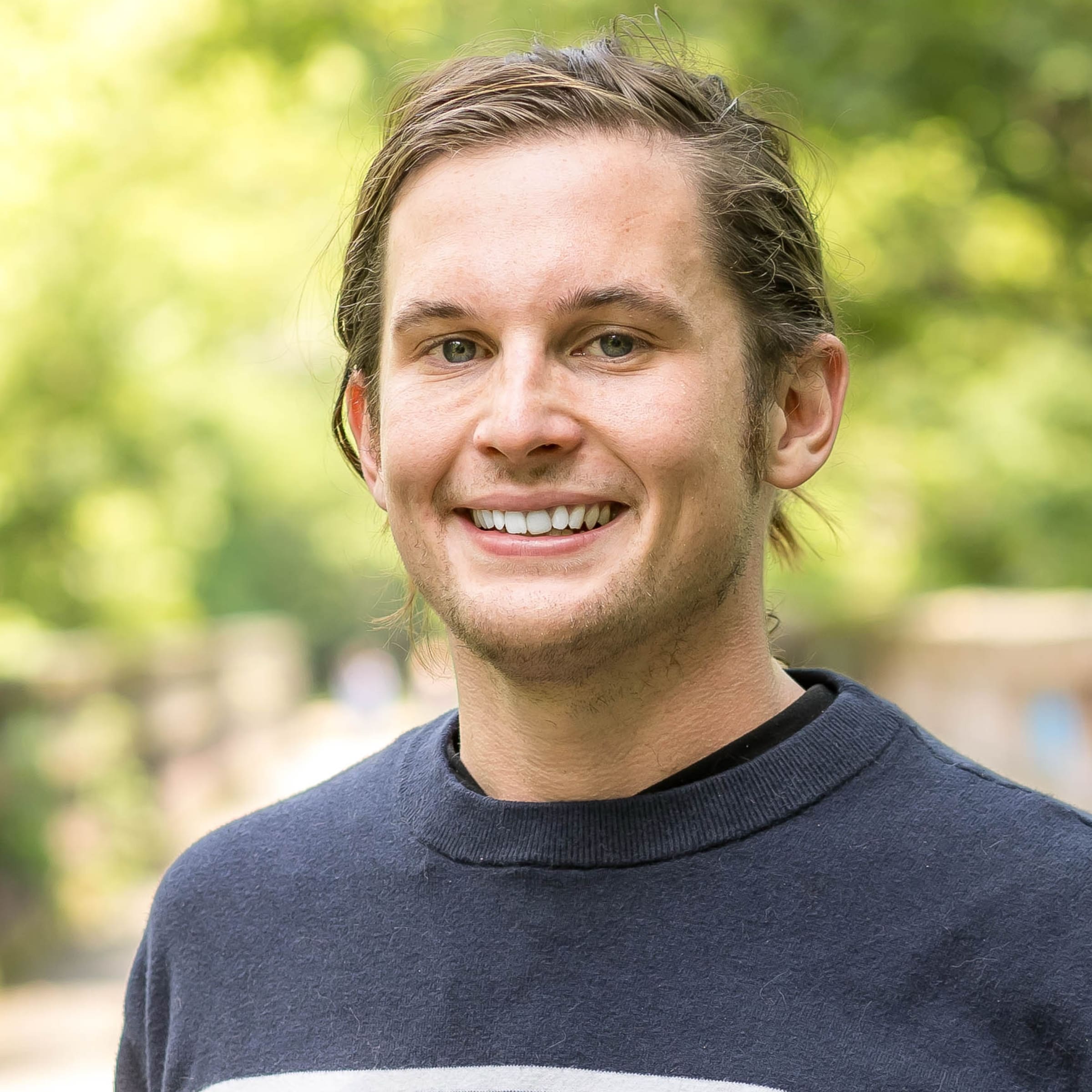 Lucas Valitski, practitioner at The Resiliency Center of Greater Philadelphia, smiling outdoors in front of a soft-focus green park background.