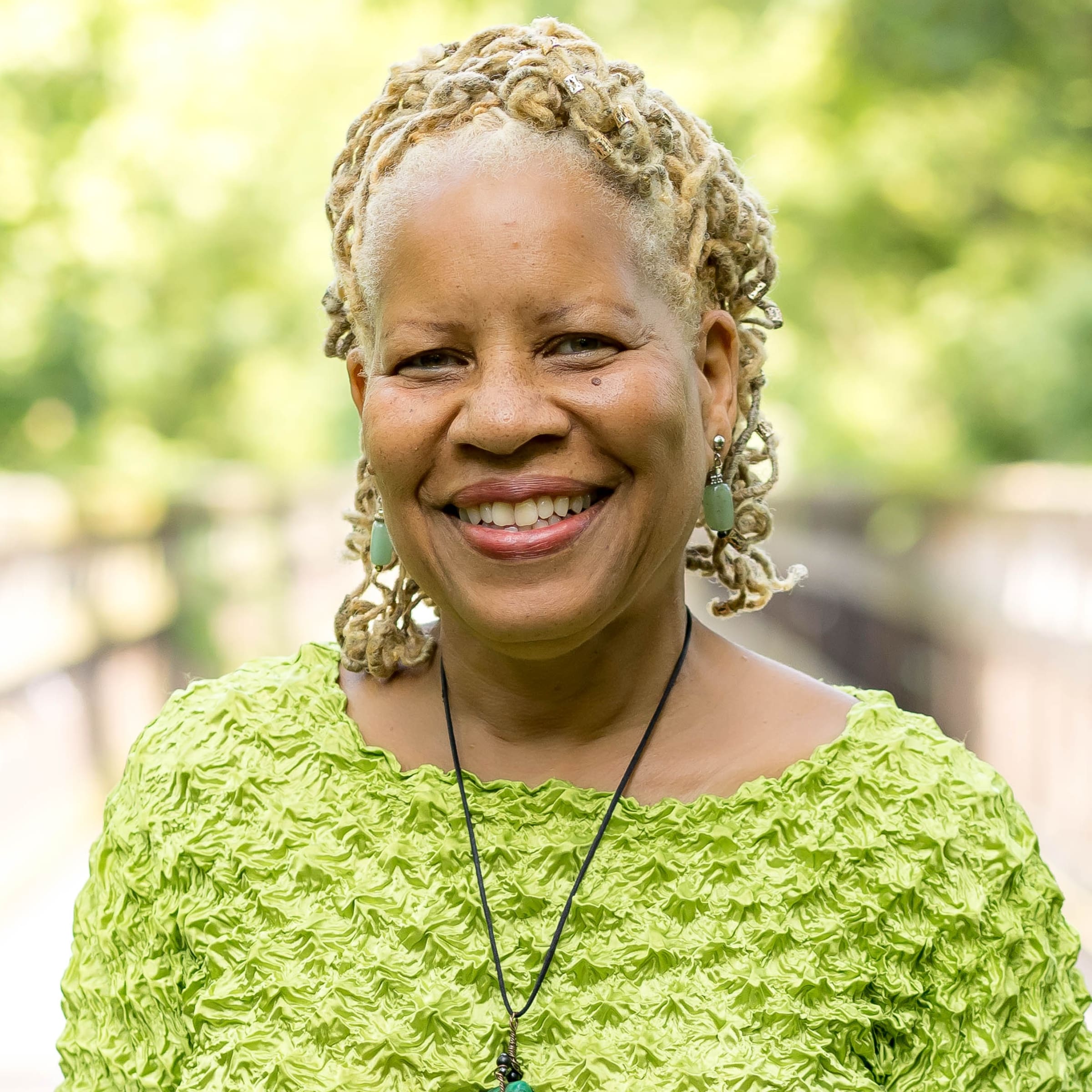 Tracey A. Smith, practitioner at The Resiliency Center of Greater Philadelphia, smiling outdoors in front of a soft-focus green park background.