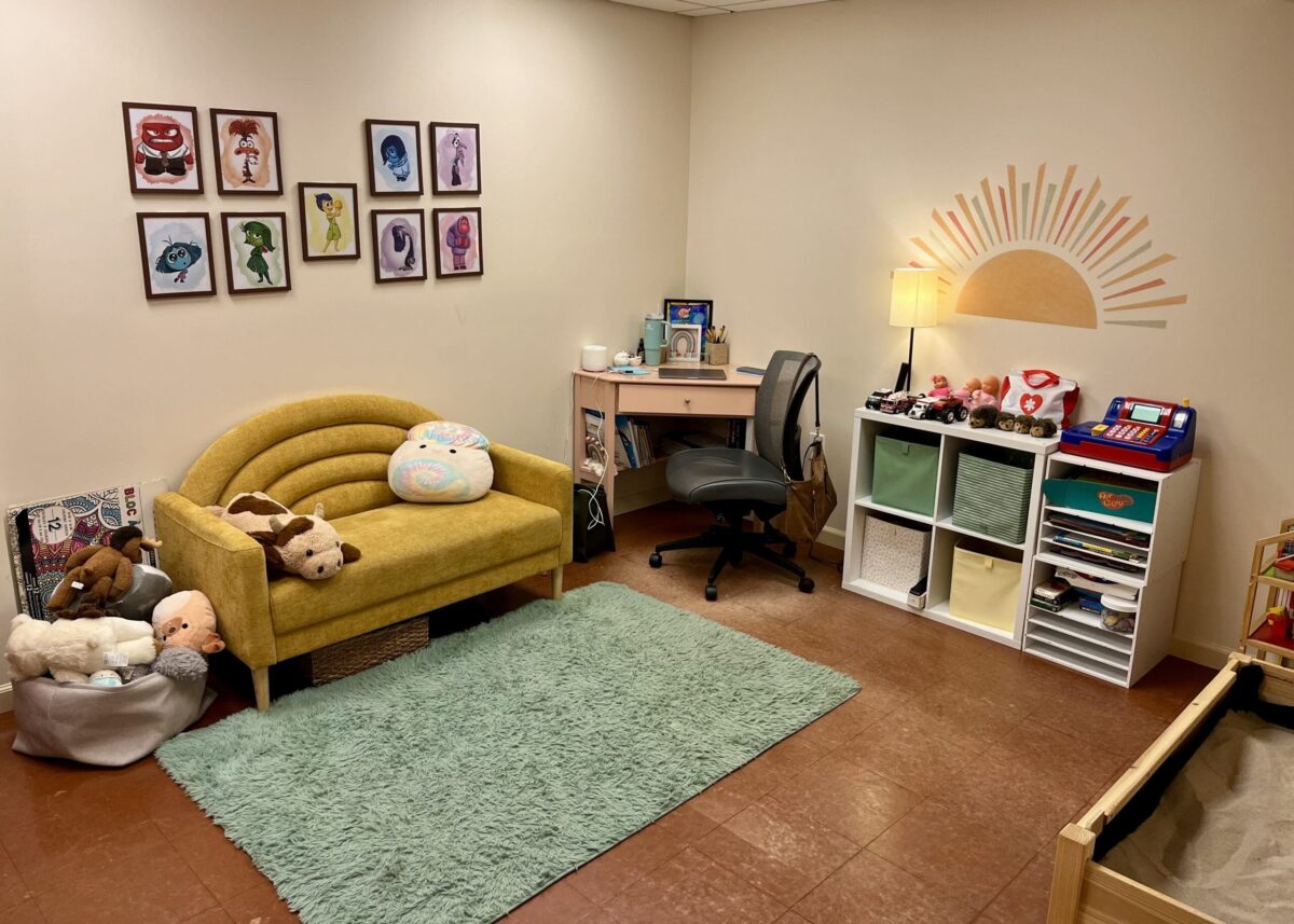 Cozy playroom with yellow sofa, stuffed animals, pastel wall art, desk, and toy shelves.