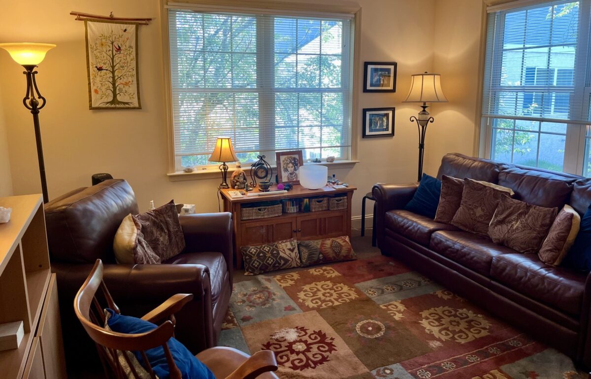Cozy office with two leather sofas, rug, lamps, and large windows showing greenery.
