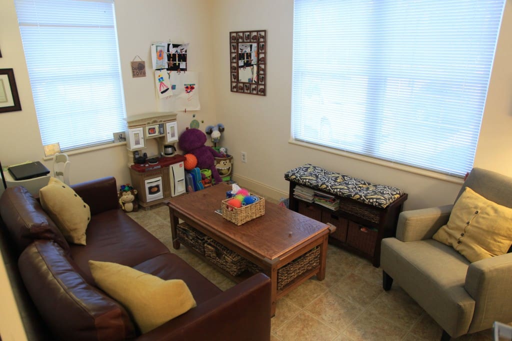 Cozy office with brown leather sofa, beige chair, wooden coffee table, and toy kitchen set area.
