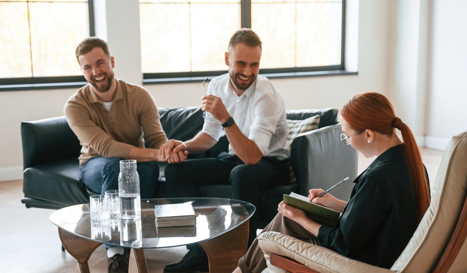 Two men sitting together on a therapy couch, laughing during a consultation session