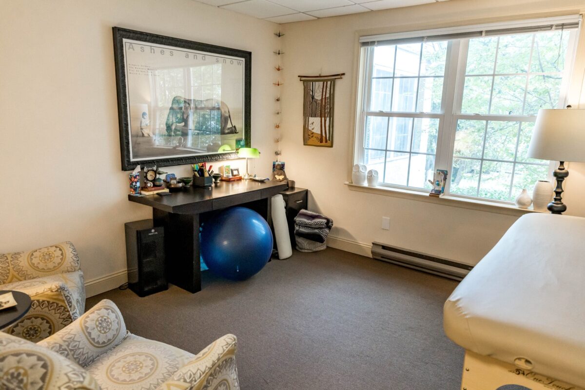 Brittiney George's Rubenfeld Synergy office with patterned armchairs, a desk, and a bodywork table.
