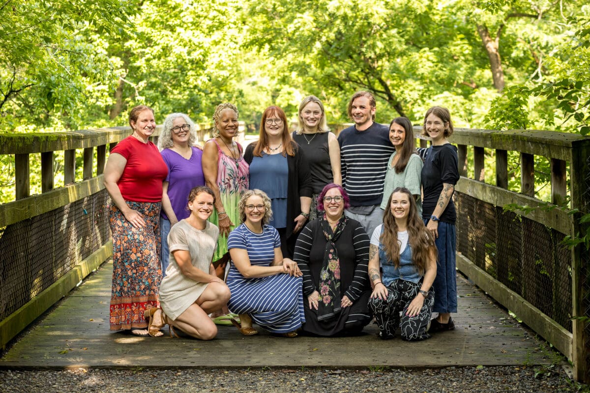 The practitioners of The Resiliency Center gathered together on a wooden footbridge surrounded by summer greenery