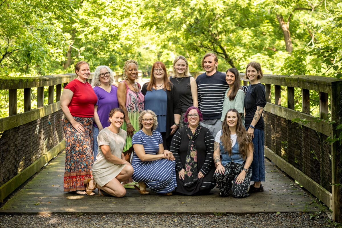 The practitioners of The Resiliency Center gathered together on a wooden footbridge surrounded by summer greenery