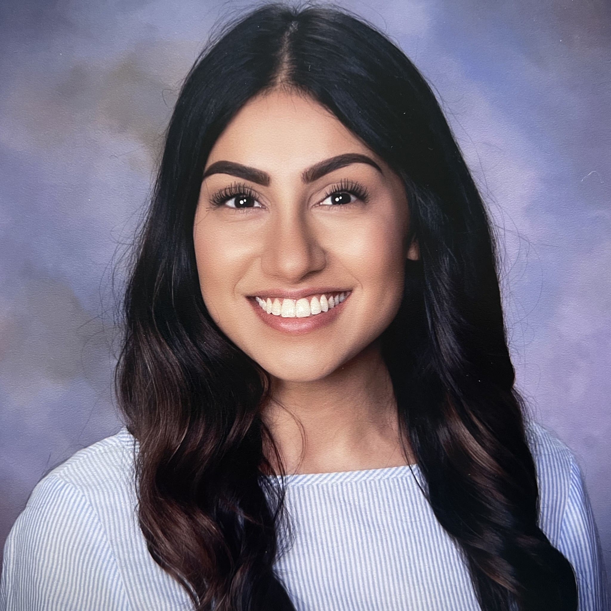 Nadia Hassanali, practitioner at The Resiliency Center of Greater Philadelphia, smiling in front of a soft blue-violet studio backdrop.